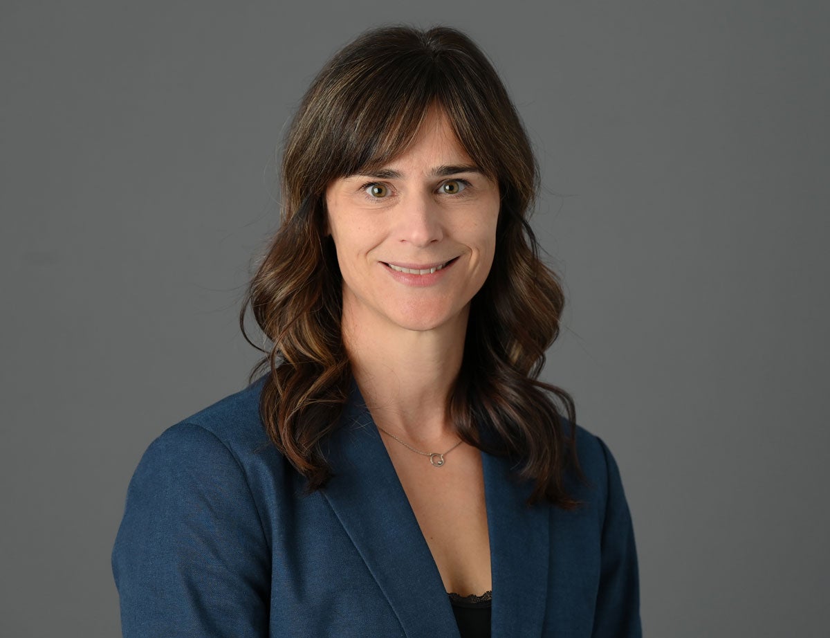 A portrait photo of a woman with long brown hair and short banks wearing a blue dress jacket