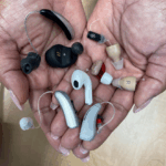 A pair of hands holds a variety of different hearing aids