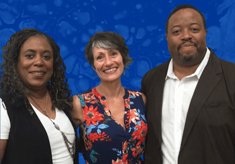 A Black woman with long curly hair stands next to a white woman with short dark gray hair who stands next to a Black man with short dark hair and mustache