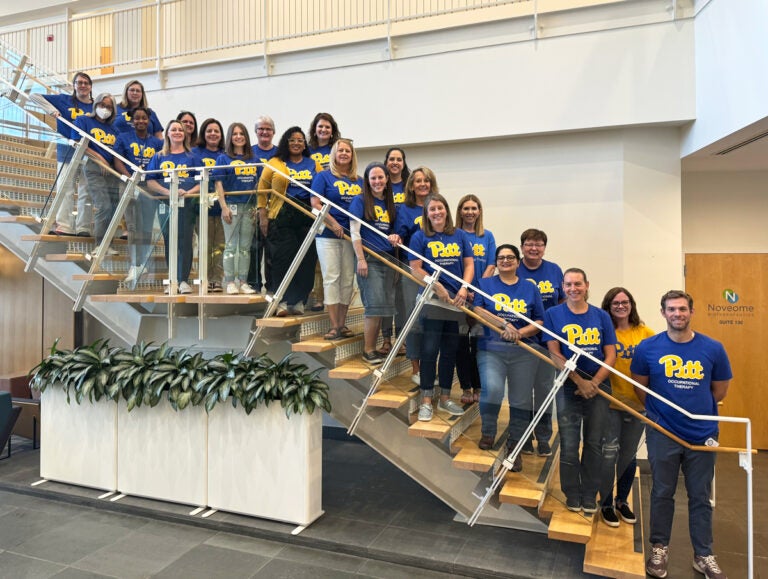 A large group of people wearing blue and gold Pitt t-shirts pose on a stairwell.