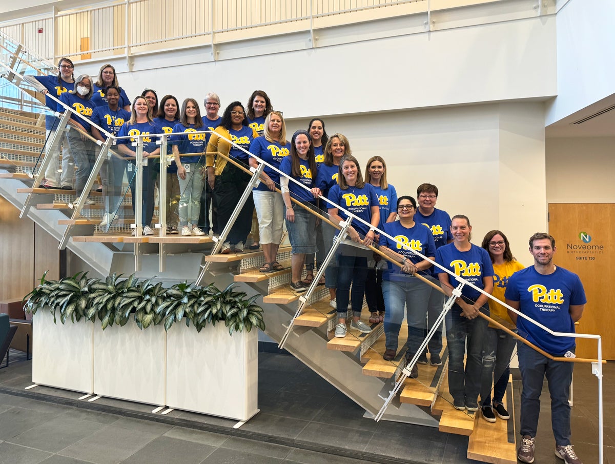 A large group of people wearing blue and gold Pitt t-shirts pose on a stairwell.