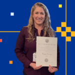 A woman with long blonde curly hair holds a large ornate certificate with her name