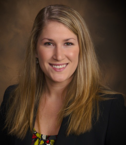 A woman with long blonde hair wears a dark jacket and colorful top
