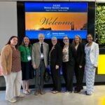A group of seven people stand in front of a conference welcome sign