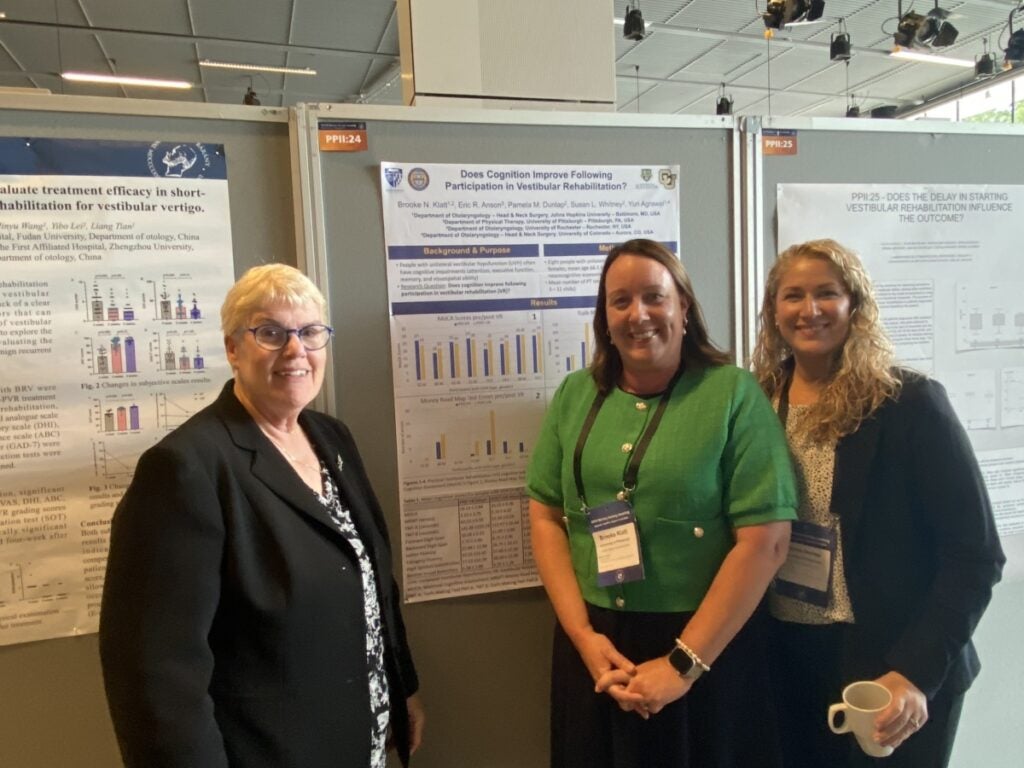 Three women stand in front of a research poster presentation