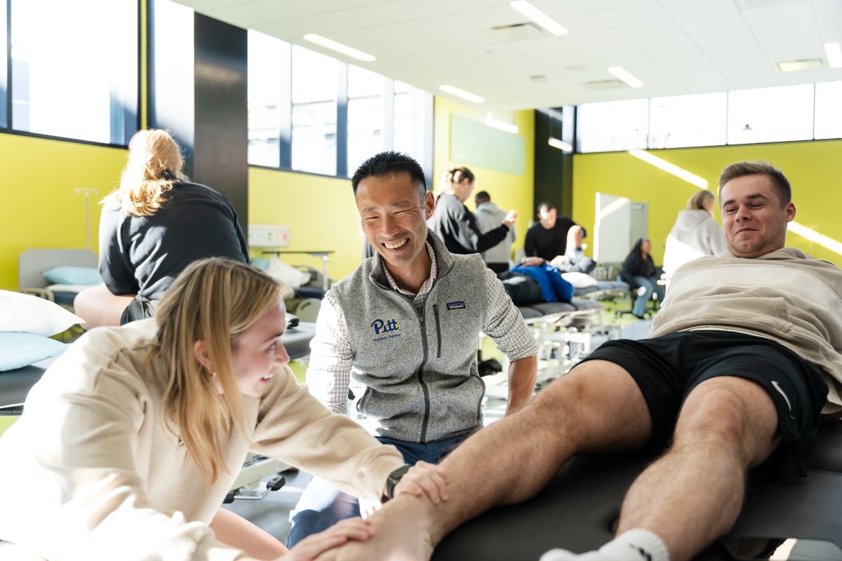 Students in a clinical classroom examine patients while an instructor looks on