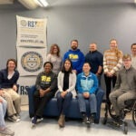 A group of people sitting and standing together near a sign that reads "Rehabilitation Science and Technology Continuing Education."