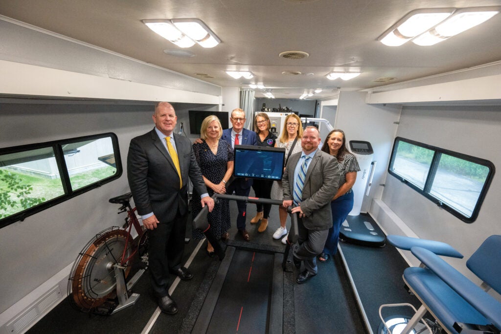 A group of men and women dressed formally standing inside a mobile research vehicle (MRV) next to exercise equipment.