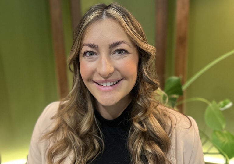 A woman with brown and blonde curled hair wearing a tan blazer over a black top.