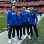 A man with short brown hair, a woman with brown hair pulled back, a man with short light hair and a man with brown hair pulled back all wearing black pants and blue sweatshirts that have the Los Angeles Rams logo on them.
